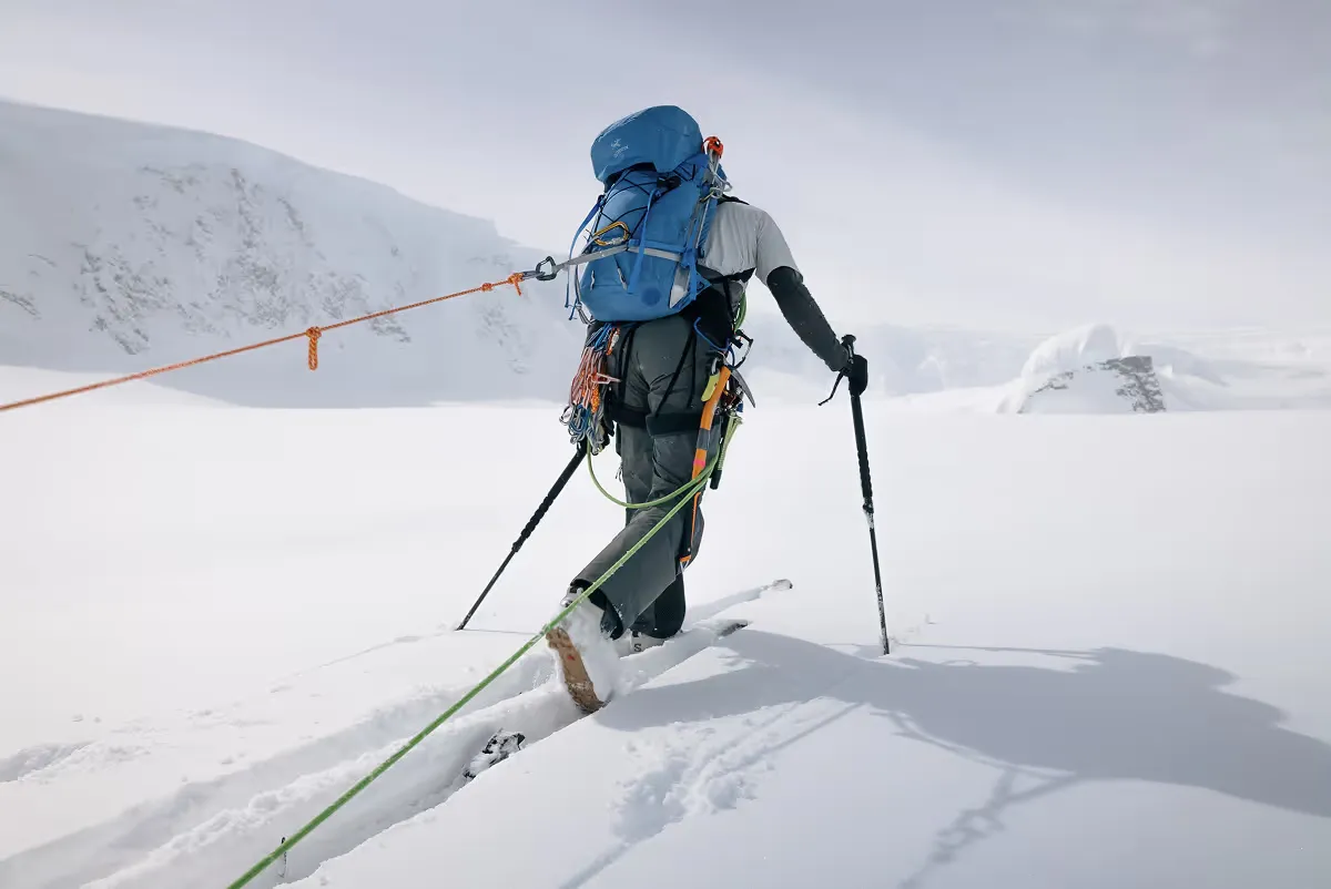 Mountaineer ascending snowy slope with blue backpack and climbing gear