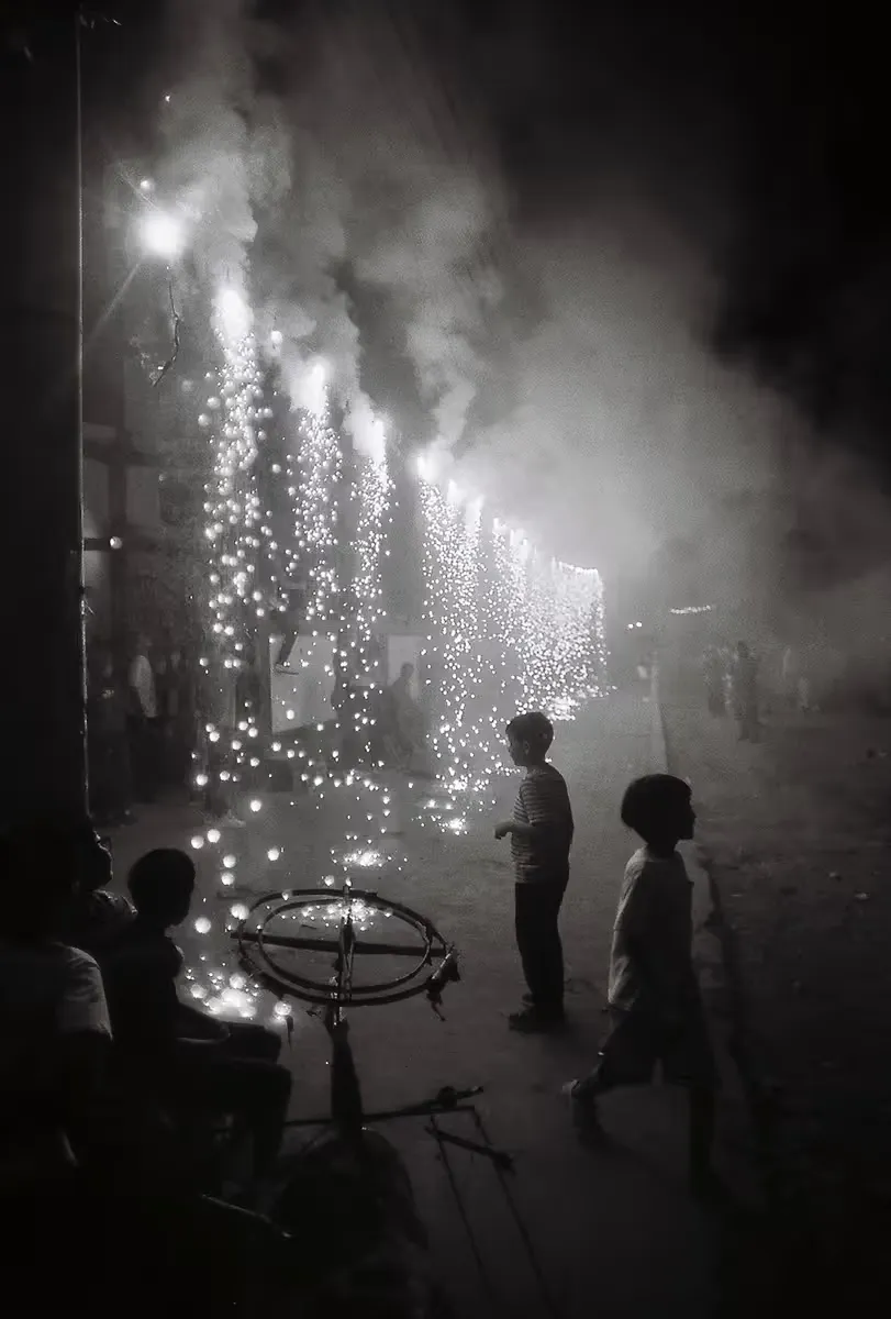 Children watching fireworks cascade with sparks and smoke in night street