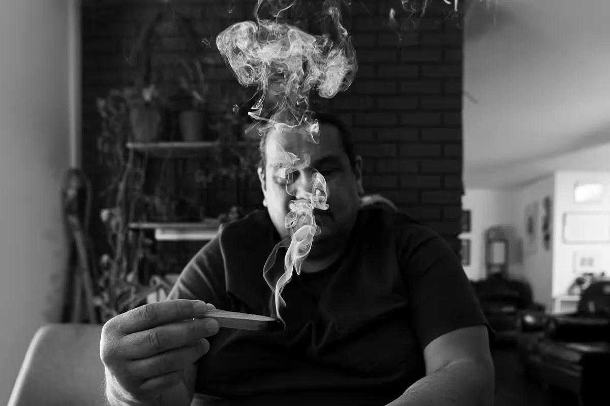 Person holding burning incense stick with smoke rising indoors