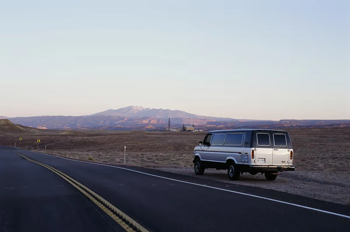 Vintage van parked on desert highway shoulder with mountains at dusk