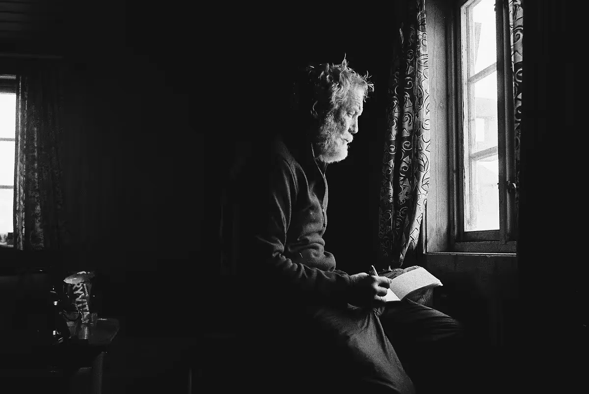 Geoff reading book by ornate window in darkened room